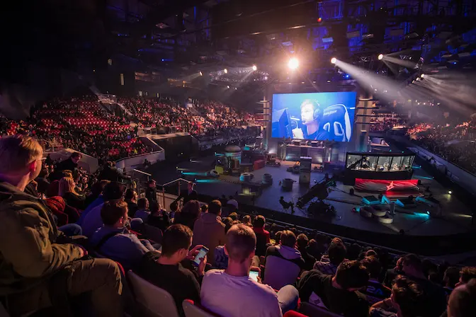 Photographie d'une compétition gaming avec un publique et un gros écran au centre de la scène ou on y voit un gamer